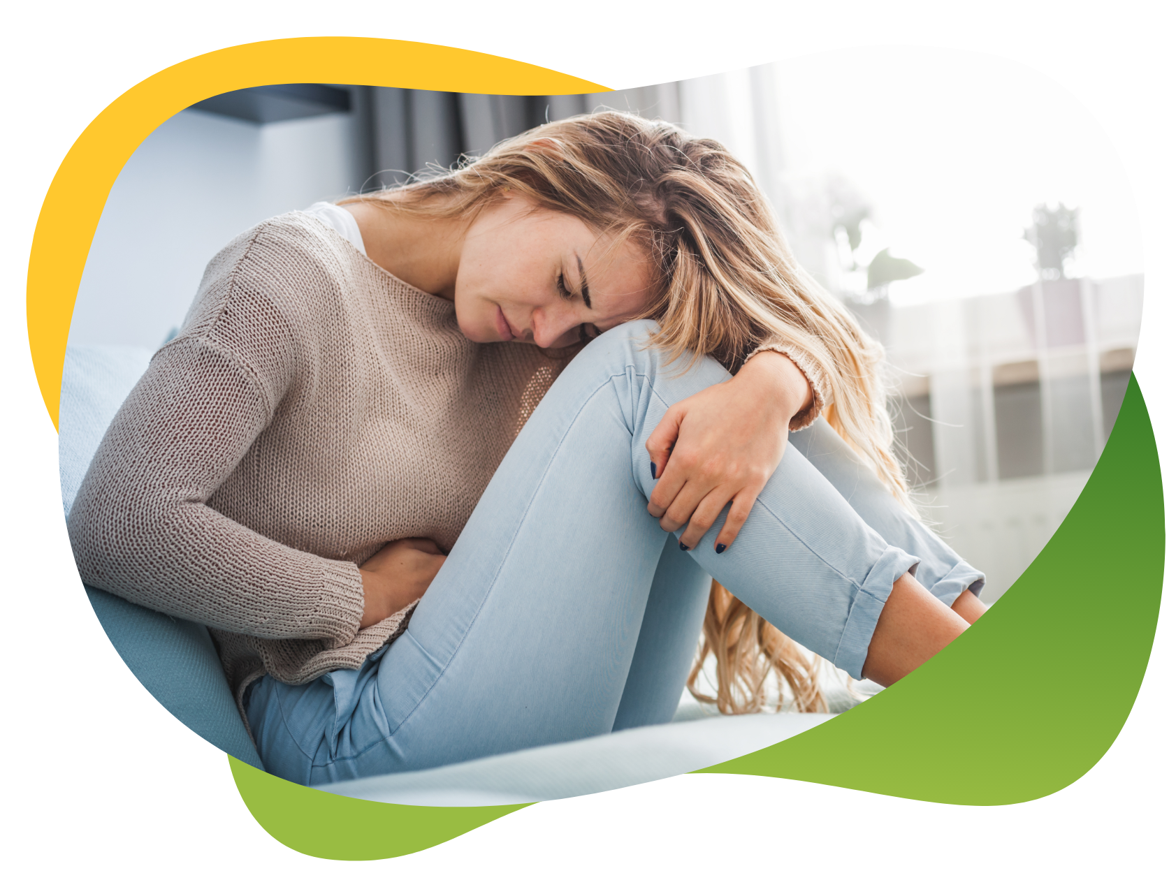 Mladá žena, kterou trápí nadýmání během menstruace, sedí skrčená na zemi a levou rukou se drží za břicho.