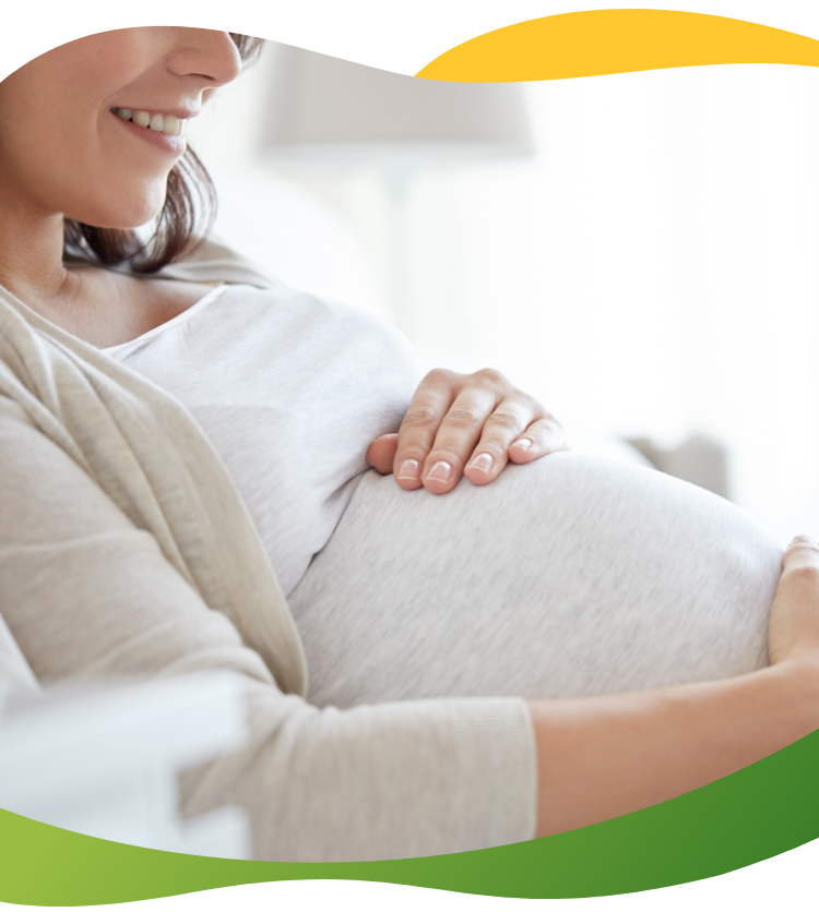 Těhotná žena, kterou netrápí nadýmání, sedí a usmívá se a přitom si hladí těhotné bříško.