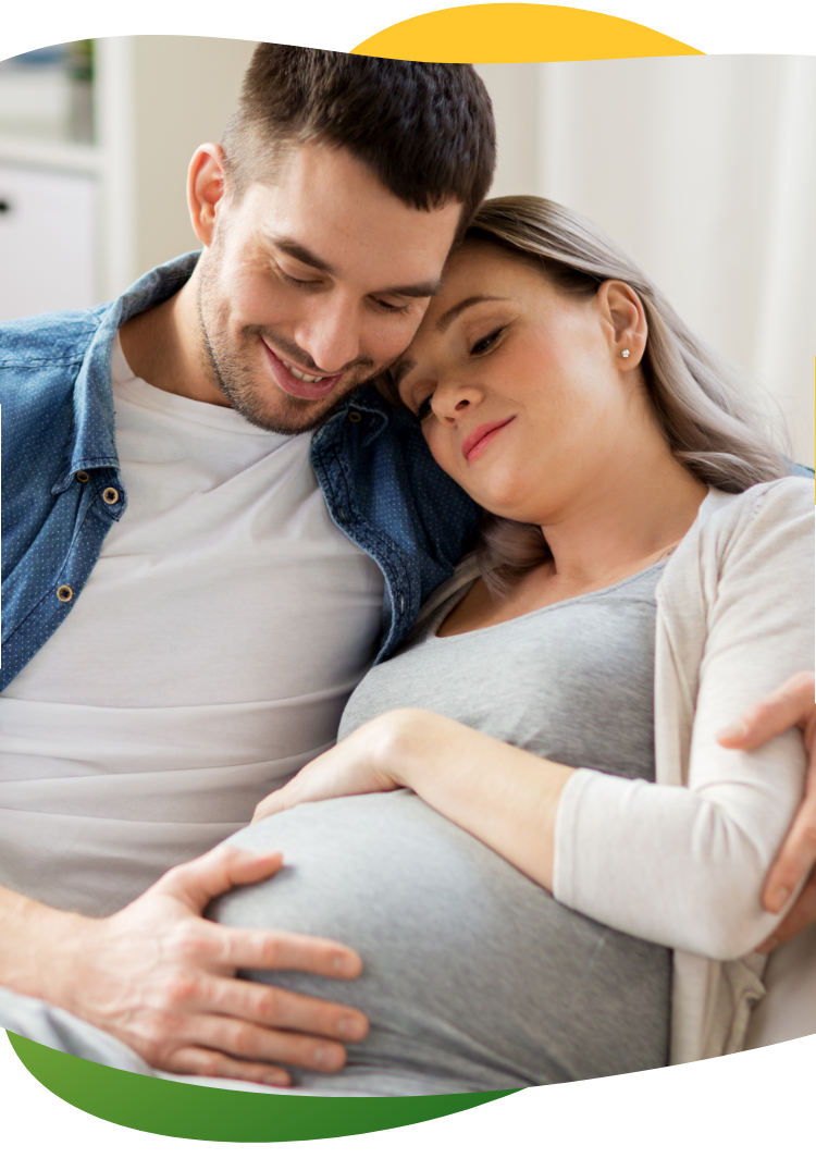 Těhotná žena, kterou trápí nadýmání, sedí na pohovce a oči má zavřené. Její partner ji utěšuje a objímá ji.