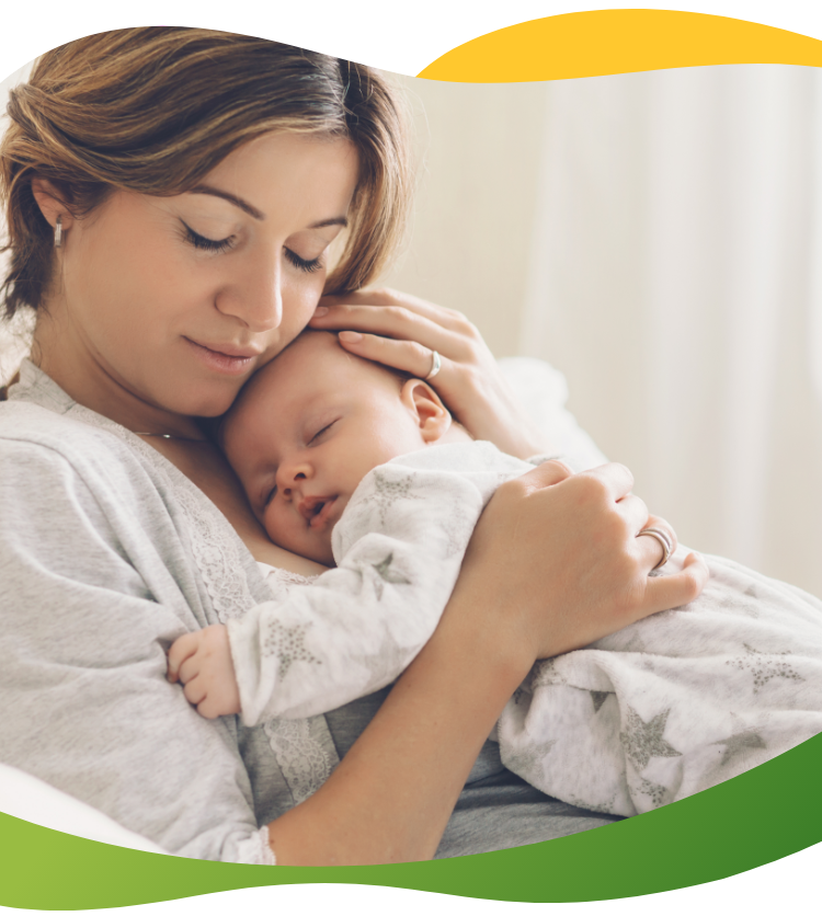 Mladá matka se zavřenýma očima, která k sobě tiskne spící miminko.